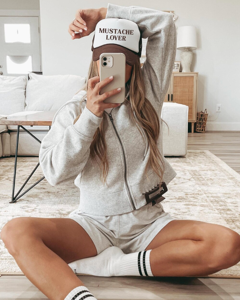 Person sitting on the floor wearing a 'Mustache Lover' cap in a modern living room.