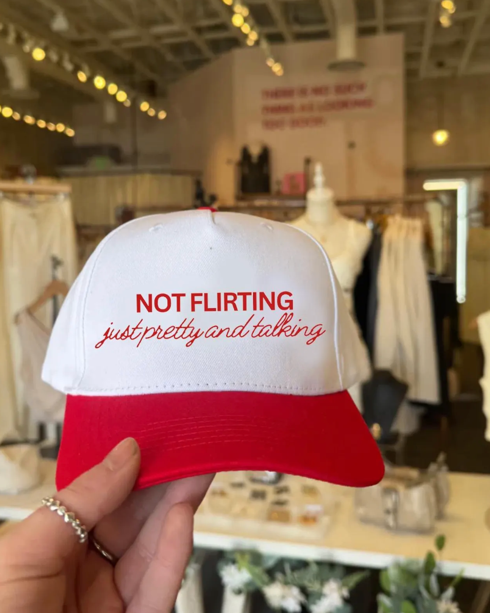 Red and white cap with text held in front of a clothing store background
