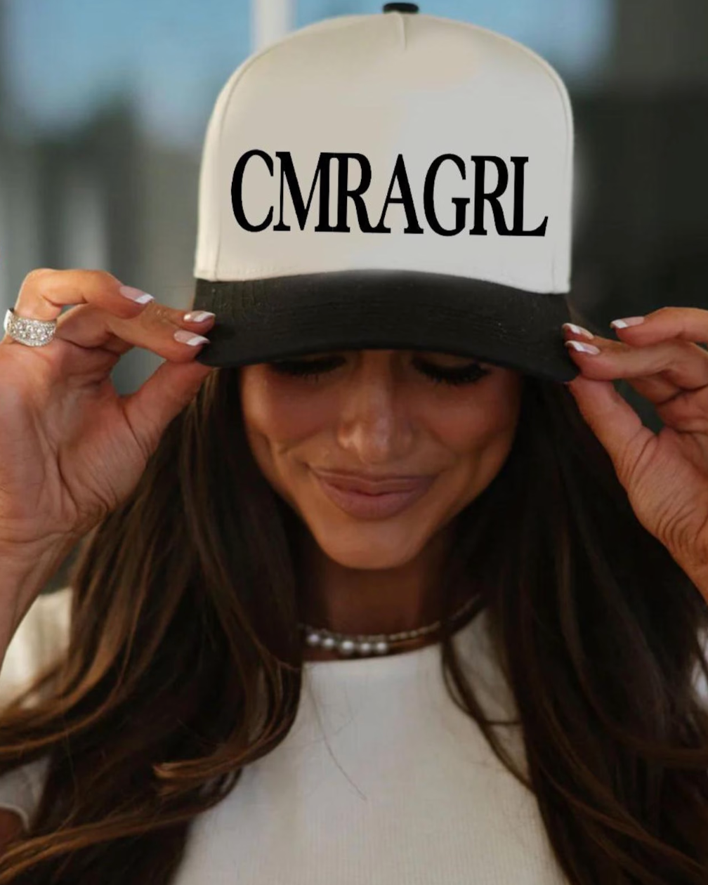 Person wearing a cap with 'CMRAGRL' text, blurred background