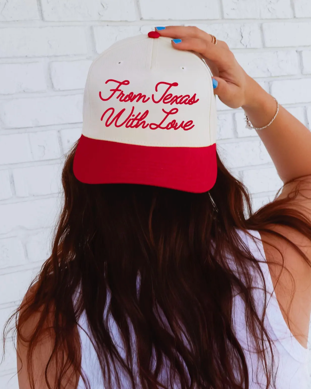 Person holding a cap with 'From Texas With Love' text against a white brick wall.
