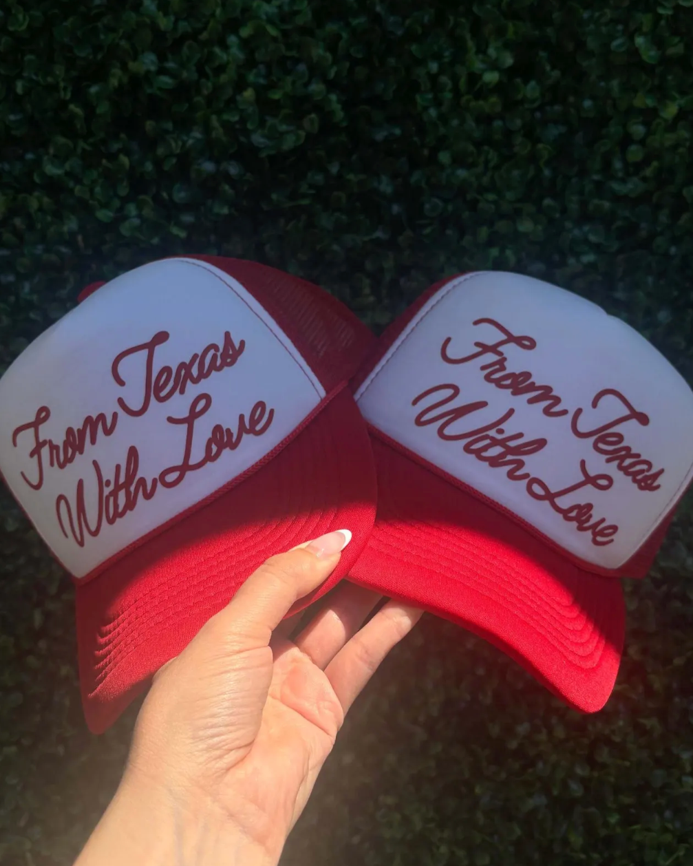 Two red and white caps with 'From Texas With Love' text held against a dark background.