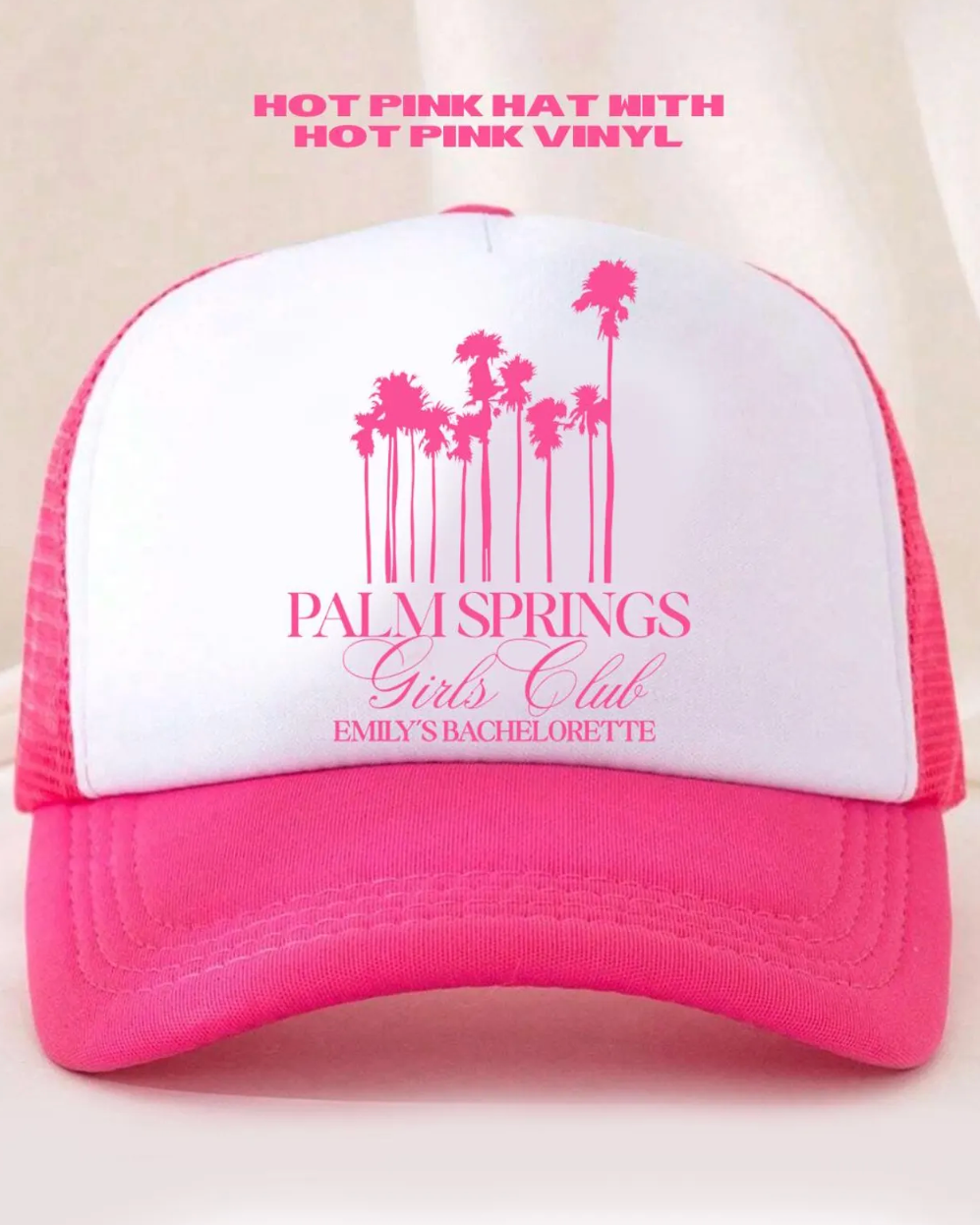 Pink and white cap with palm tree design and text on a beige background