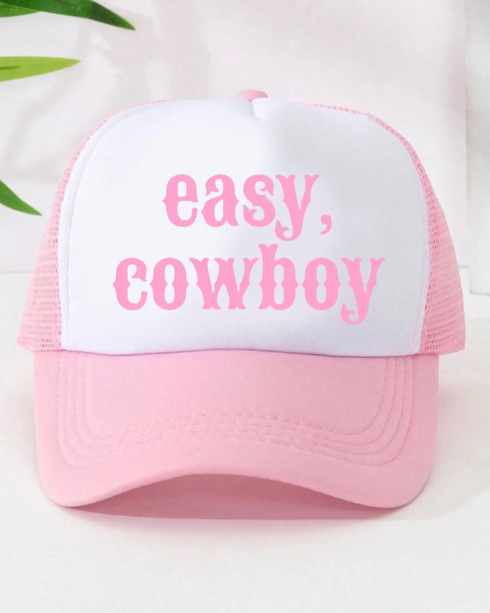 Pink and white trucker hat with 'easy, cowboy' text on a light background
