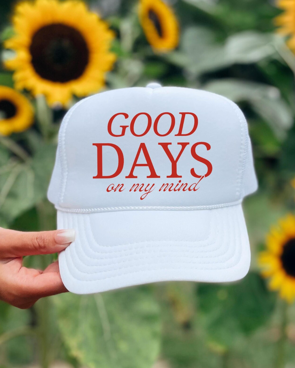 White cap with 'Good Days on my mind' text held in front of sunflowers