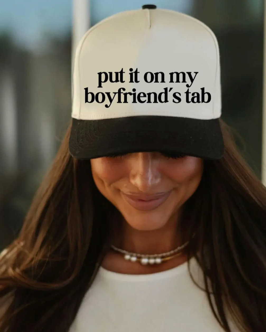 Person wearing a cap with text 'put it on my boyfriend's tab' against a blurred background