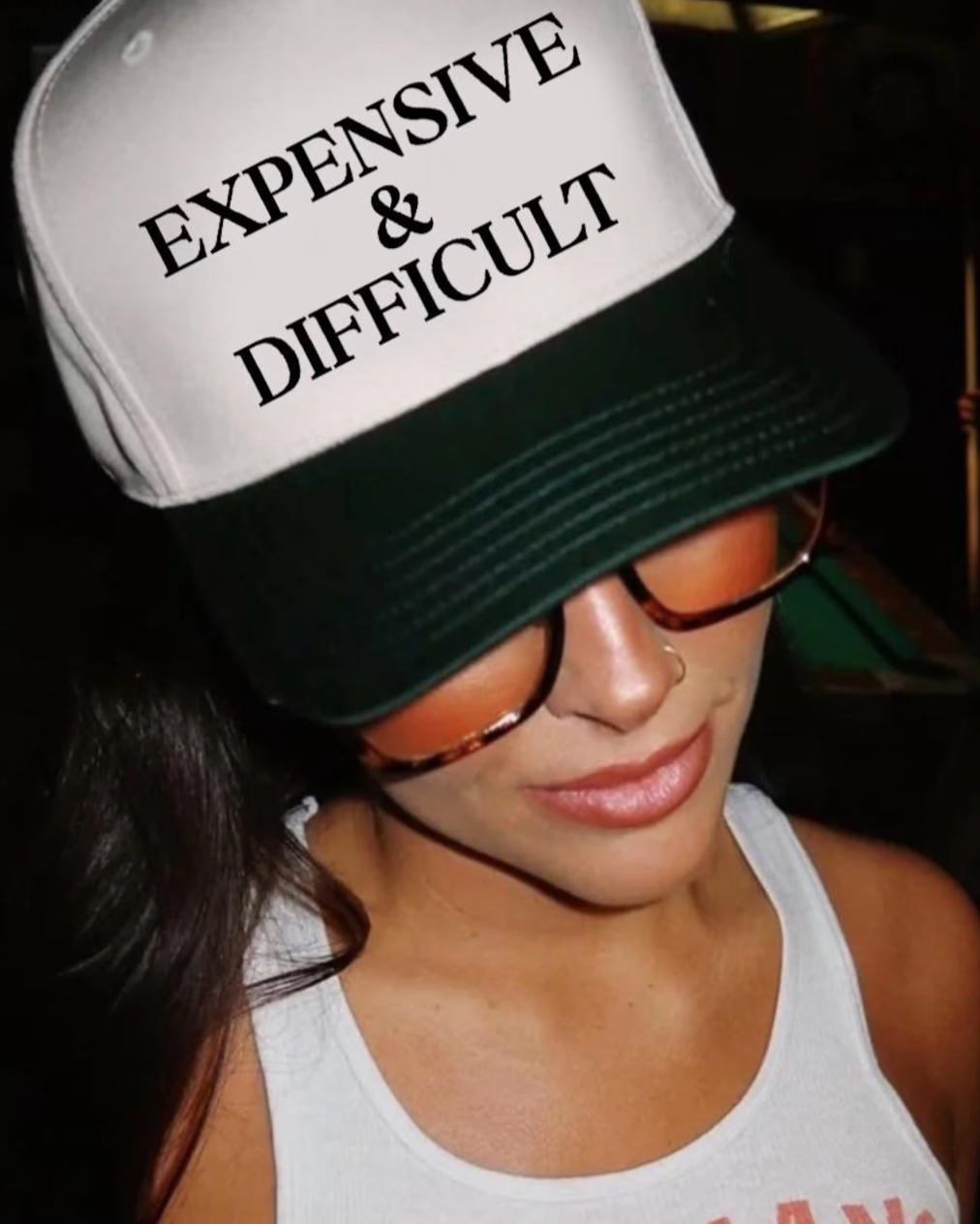 Person wearing a cap with 'EXPENSIVE & DIFFICULT' text, sunglasses, and white tank top.
