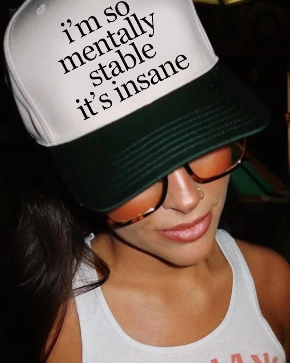 Person wearing a cap with text 'i'm so mentally stable it's insane' in a dark setting