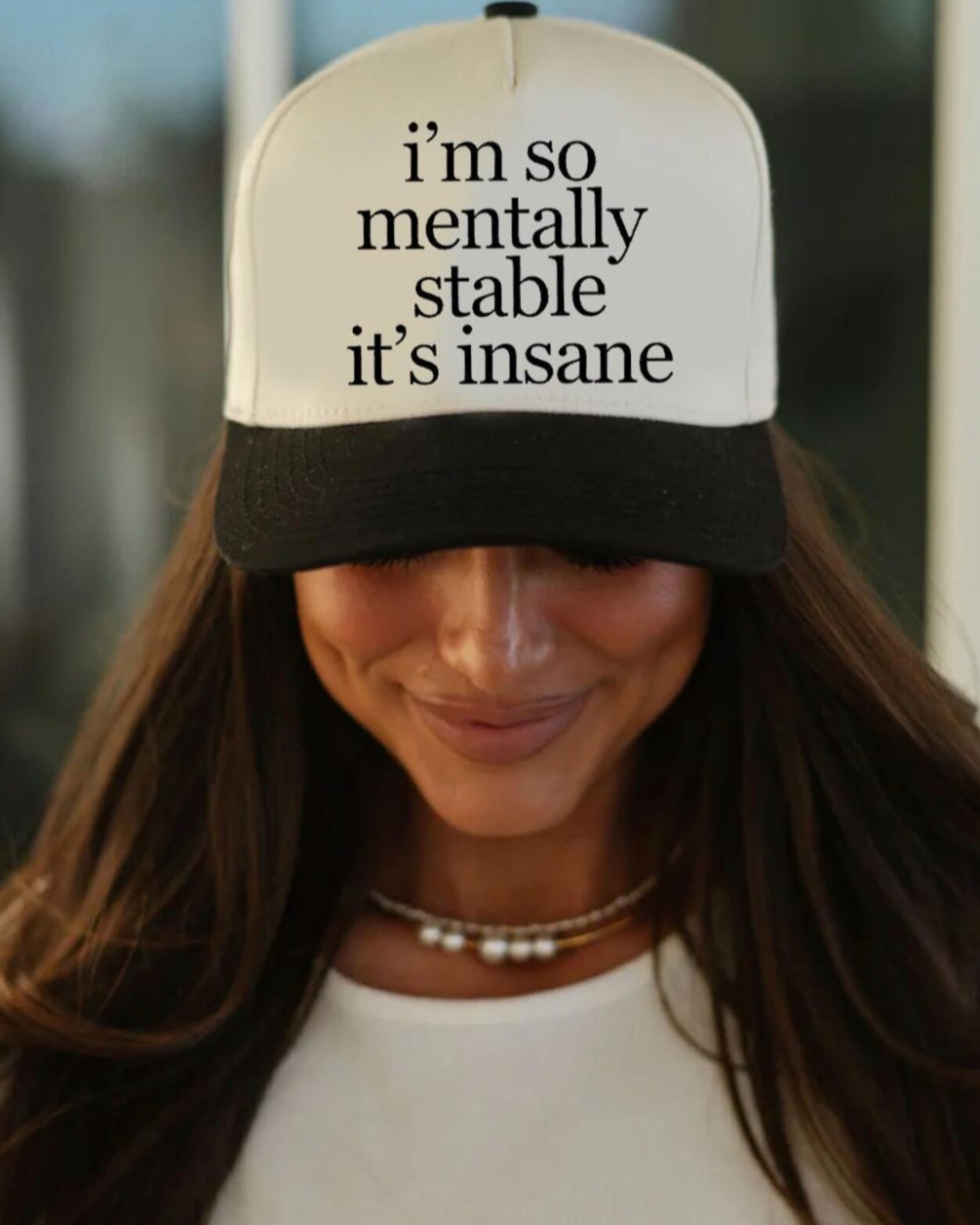 Person wearing a cap with text 'i'm so mentally stable it's insane' against a blurred background
