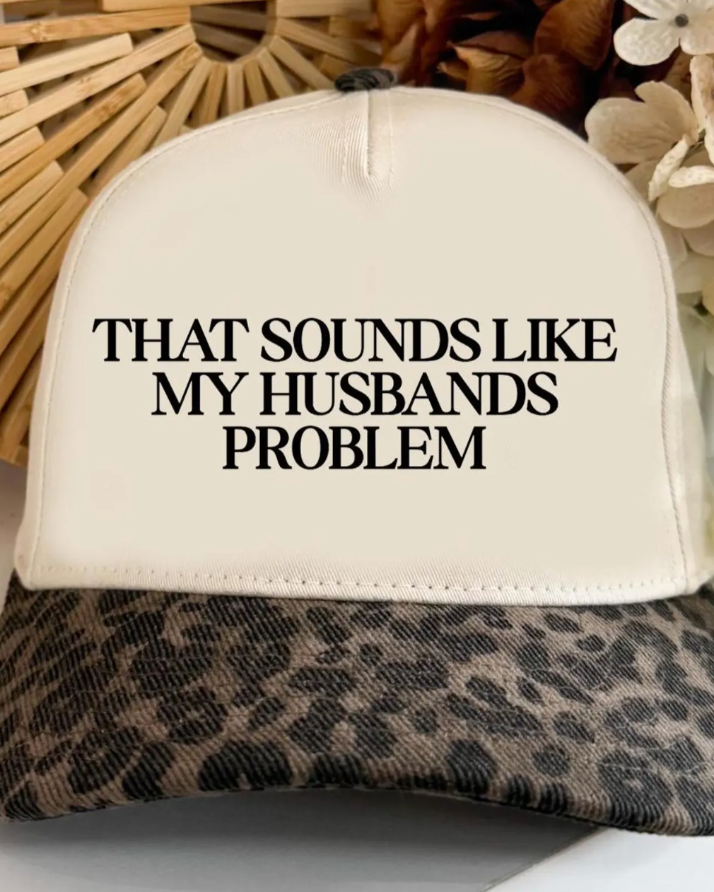 Cap with leopard print brim and text 'THAT SOUNDS LIKE MY HUSBANDS PROBLEM' on a neutral background