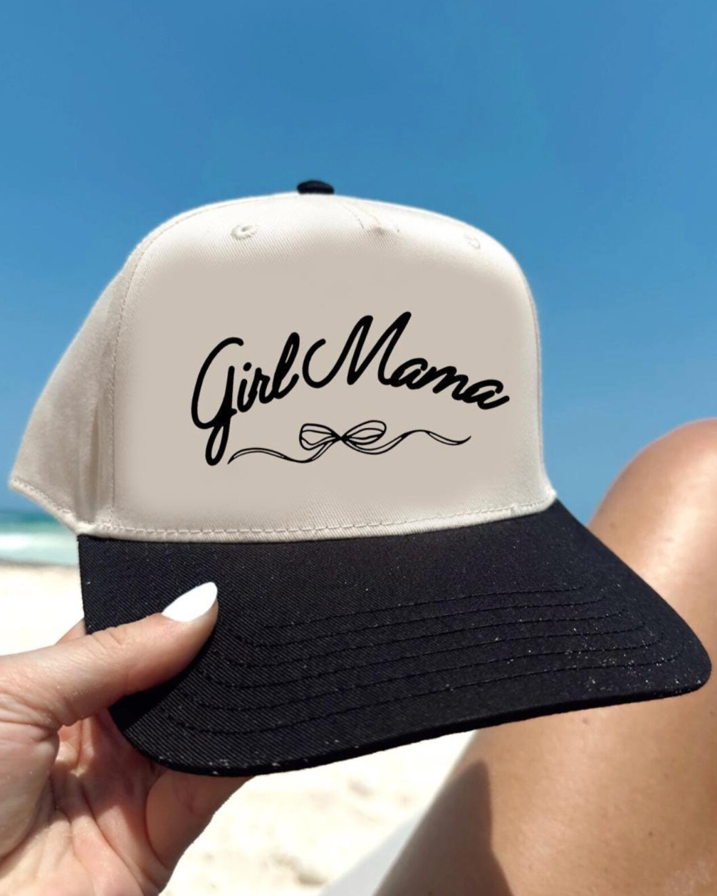 Cap with 'Girl Mama' text held by a person on a beach