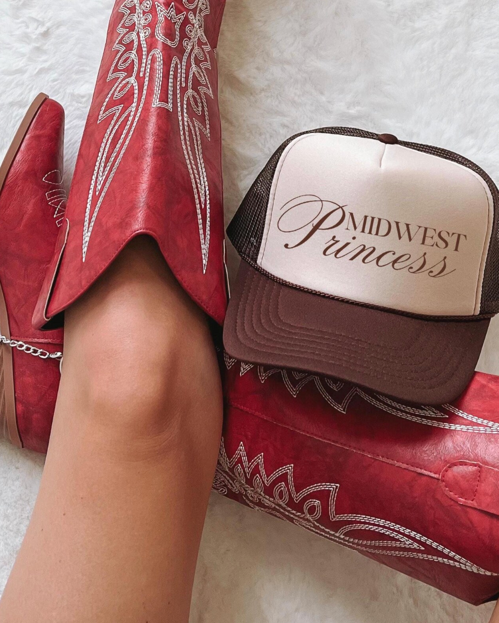 Red cowboy boots with white embroidery and a 'Midwest Princess' cap on a light background