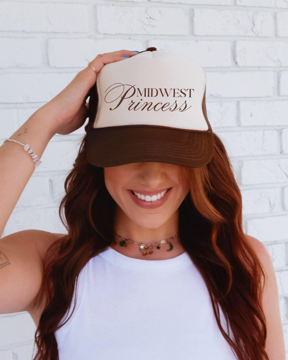 Person wearing a cap with 'Midwest Princess' text against a white brick wall
