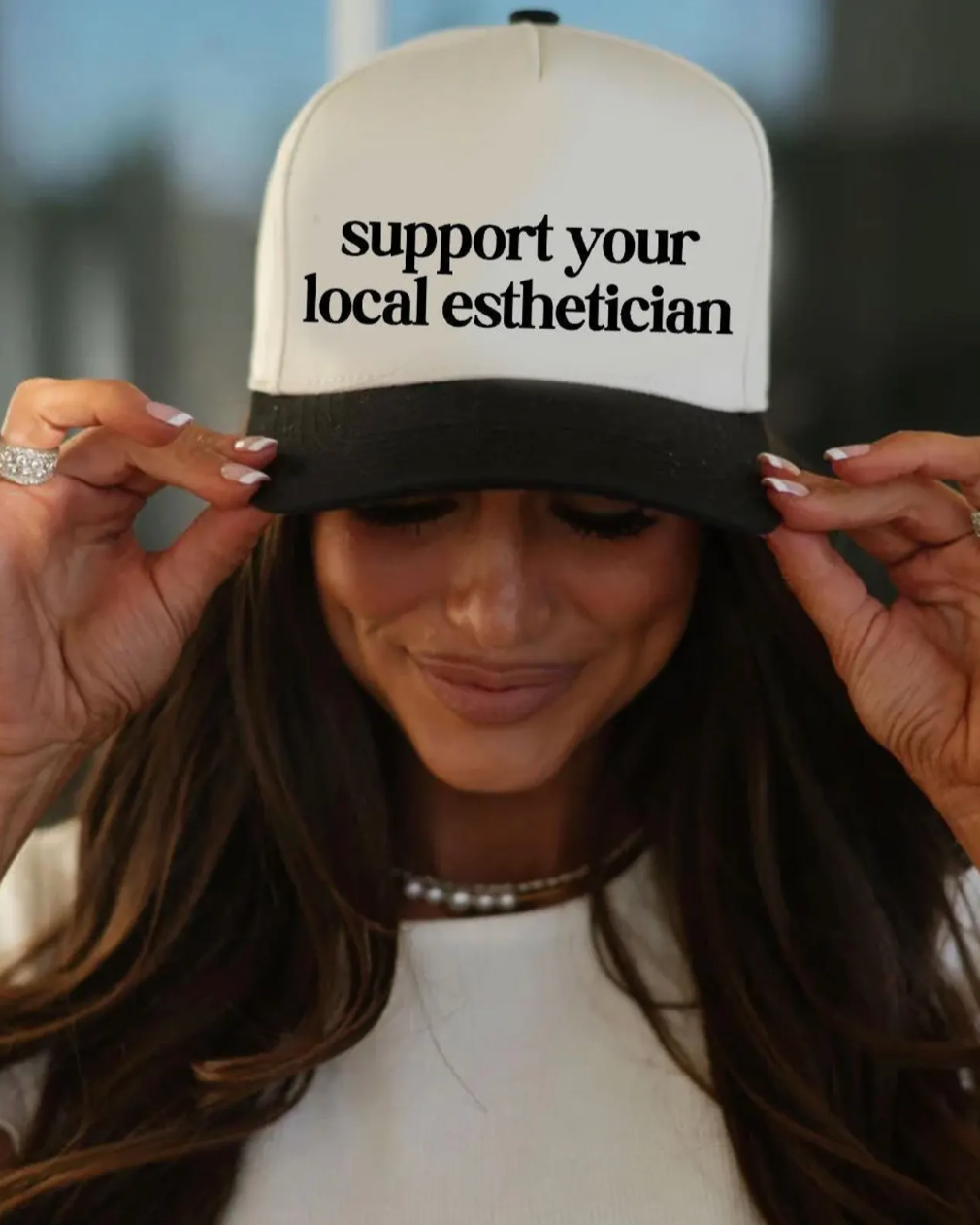 Person wearing a cap with 'support your local esthetician' text