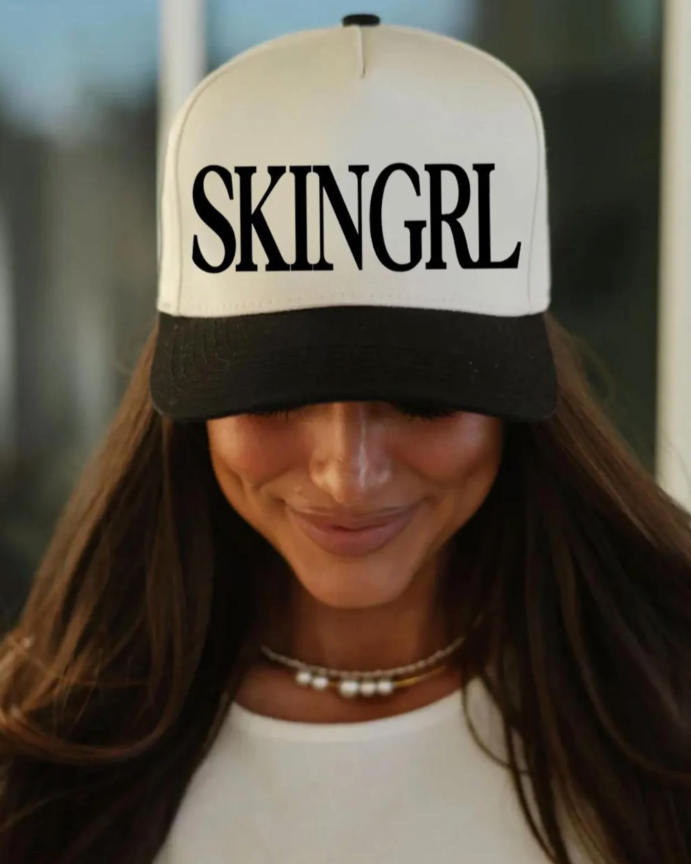 Person wearing a cap with 'SKINGRL' text against a blurred background