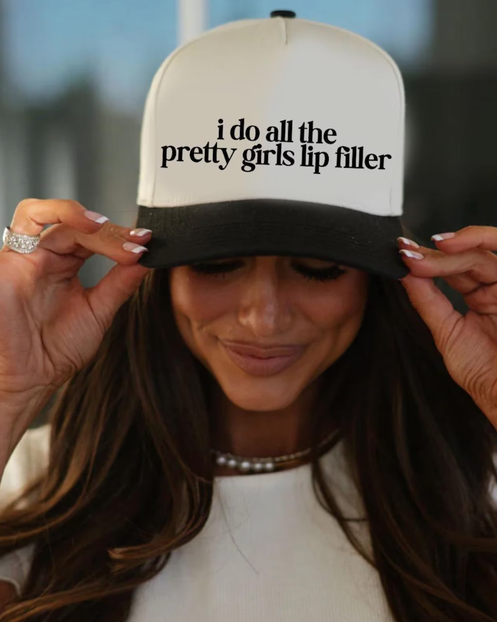 Person wearing a cap with text 'i do all the pretty girls lip filler' in an indoor setting.