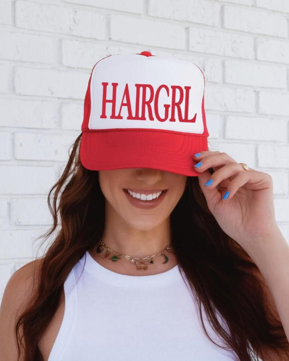 Person wearing a red and white cap with 'HAIRGRL' text against a white brick wall.