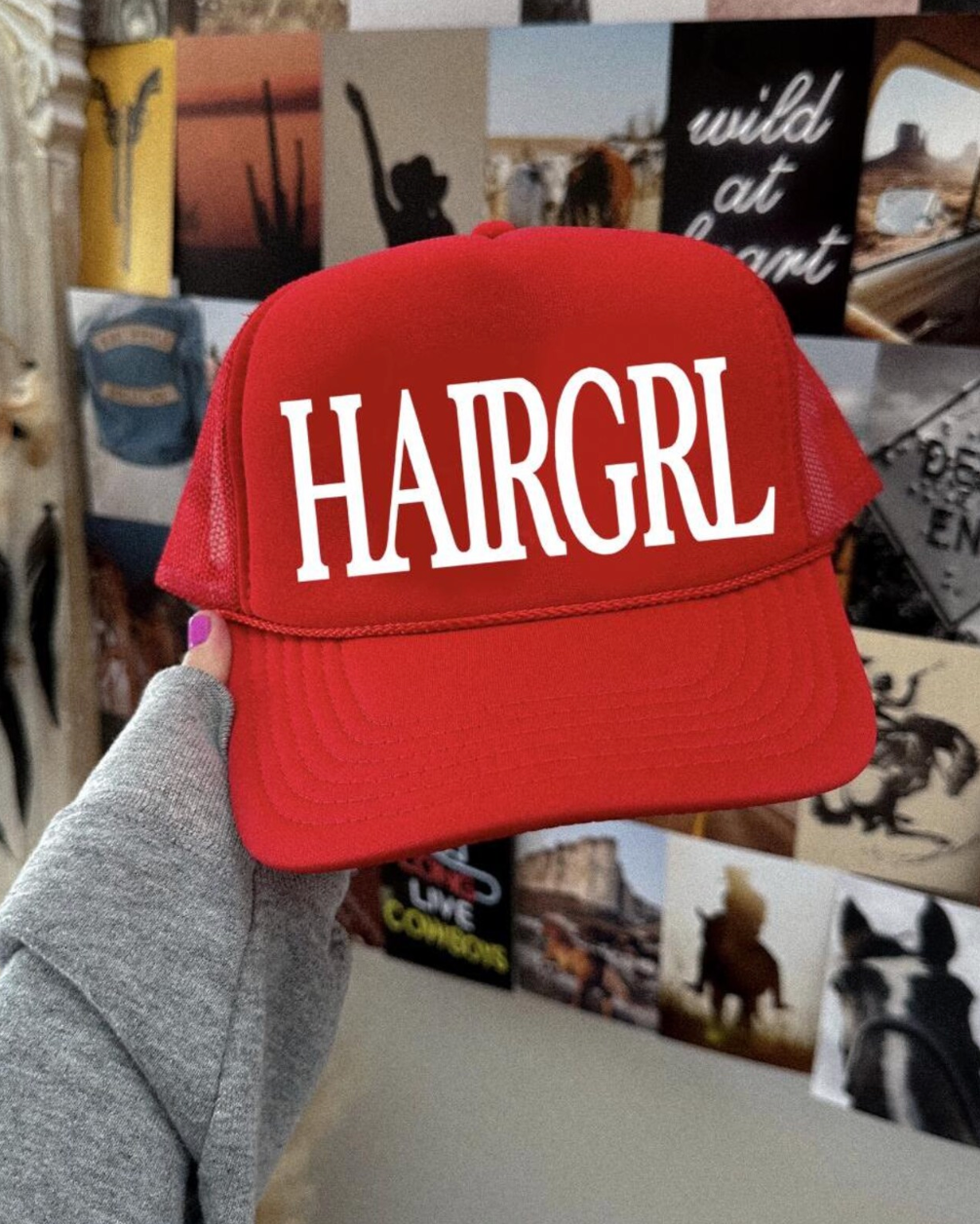 Red cap with 'HAIRGRL' text held in front of a collage of photos and posters.