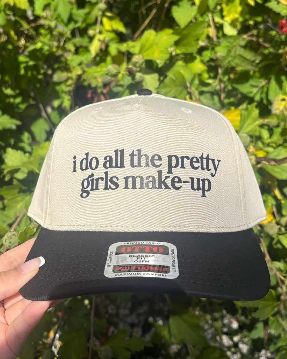 Beige and black cap with text held in front of green foliage
