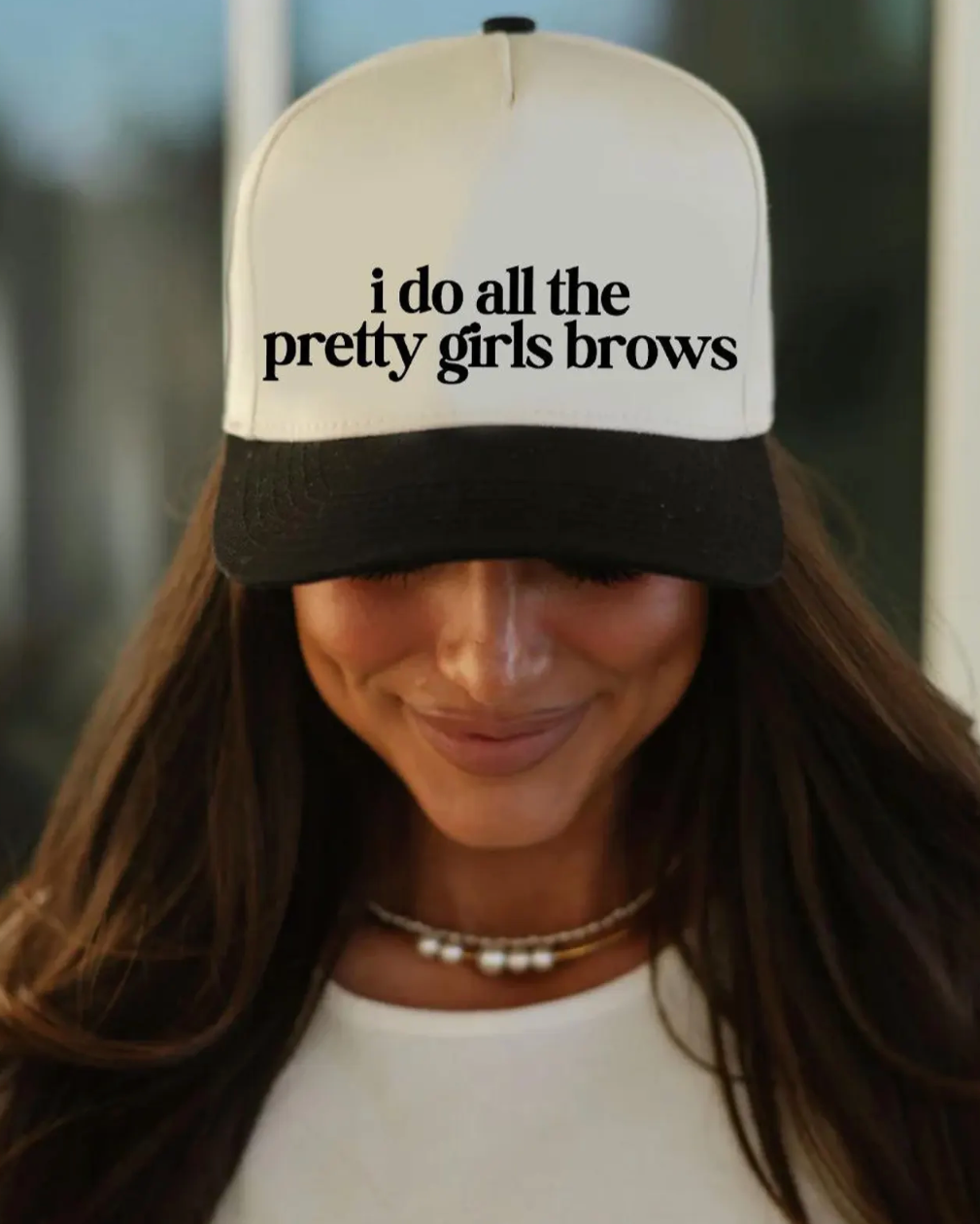 Person wearing a cap with 'i do all the pretty girls brows' text