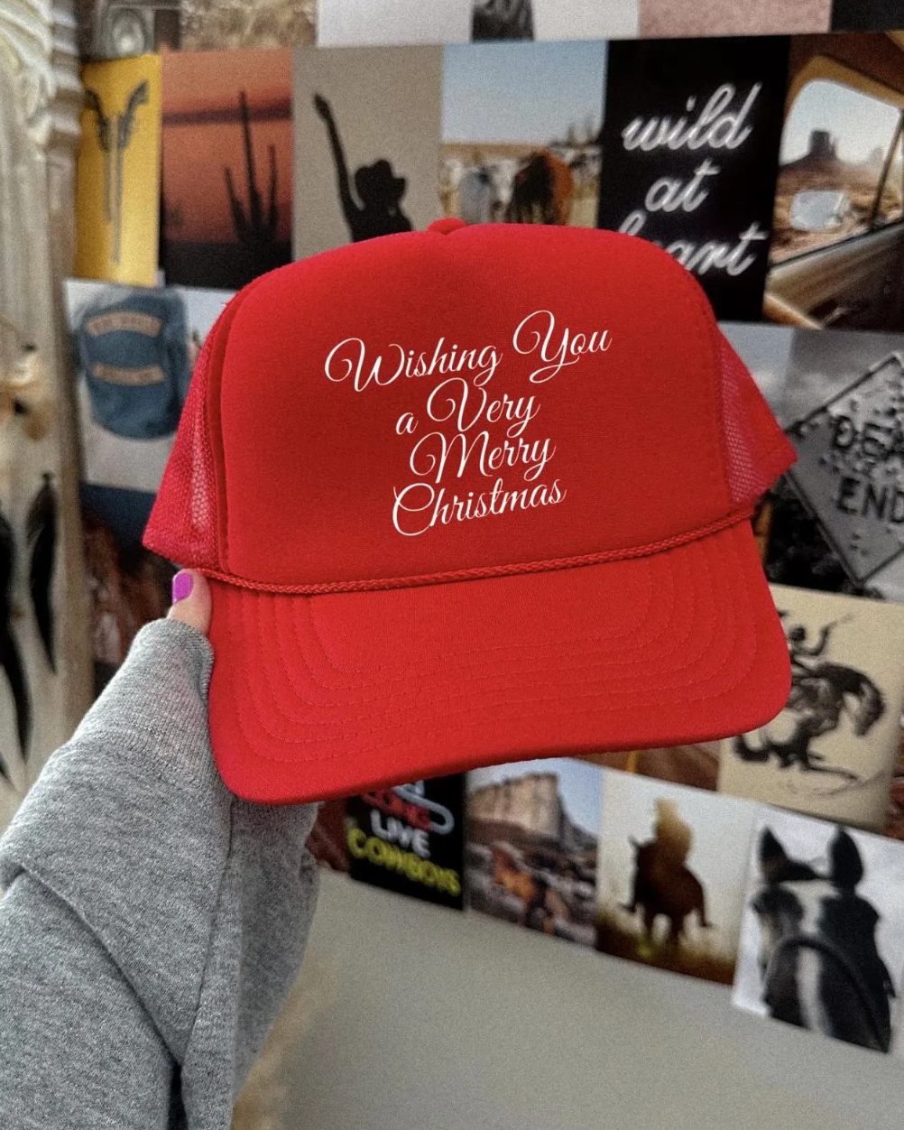 Red trucker hat with 'Wishing You a Very Merry Christmas' text held in front of a collage of photos and posters.
