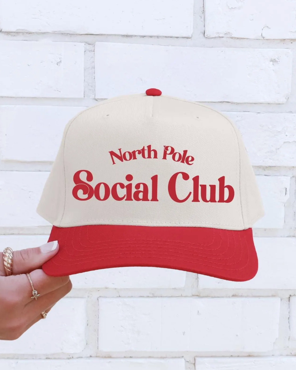 Cap with 'North Pole Social Club' text held against a white brick wall